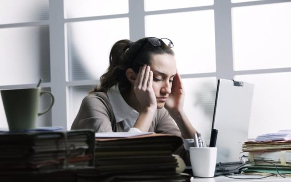 woman sitting at work office computer with headache from poor lighting